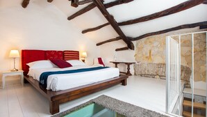 Ein Schlafzimmer mit einem hölzernen Bett, weißen Wänden, einer Steinsäule und einem Glasboden, der zu einem Balkon führt.