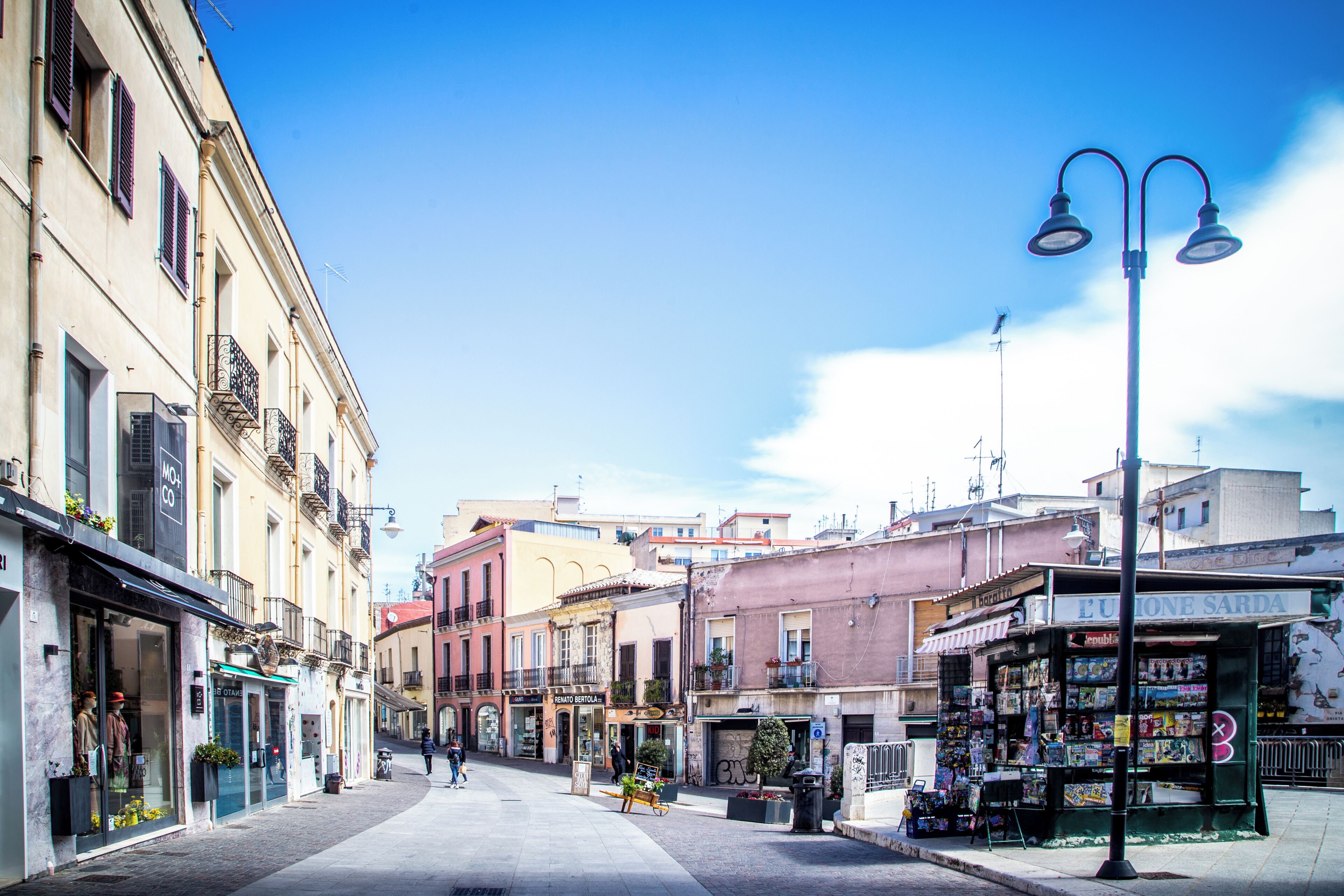 Une rue bordée de bâtiments des deux côtés, avec des boutiques et un ciel dégagé.