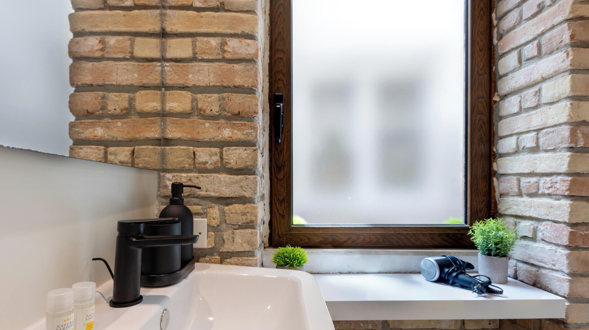 Un baño con una bañera blanca, un dispensador de jabón negro y una pequeña planta en maceta.
