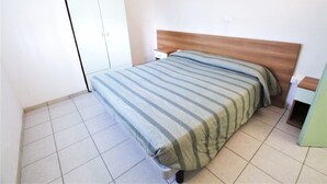 A bedroom with a bed, a nightstand, a wardrobe, and a small table. - Holiday home in Rosolina Mare (Rosolina Mare (RO))