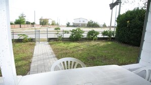 A patio area with a tiled table and chairs, a pathway, and a view of a road and buildings in the distance. - Holiday home in Rosolina Mare (Rosolina Mare (RO))
