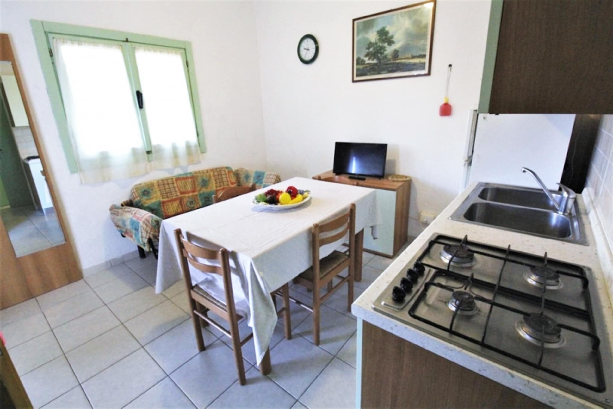 A compact kitchen with a gas stove, a sink, and a dining area with a table and chairs. A television is on a small table next to the dining area.