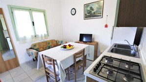A compact kitchen with a gas stove, a sink, and a dining area with a table and chairs. A television is on a small table next to the dining area. - Holiday home in Rosolina Mare (Rosolina Mare (RO))