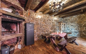 Cozy space features a stone wall, wooden beams, a refrigerator, a wooden table with benches, a chandelier, and a cabinet.