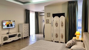 Una habitación de hotel con una cama grande, un televisor en la pared, un aparador, un armario y una lámpara.