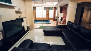 Una sala de estar con un sofá de cuero negro, un televisor de pantalla plana y un puerta de cristal que da a un patio con piscina.