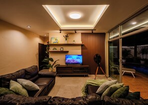 Ein modernes Wohnzimmer mit einem Flachbildfernseher, Ledersofas, einem Couchtisch und einer Glastür, die zu einem Außenbereich führt.