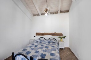 Een slaapkamer met een houten hoofdbord, een bed met een decoratieve spreideken, nachtkastjes en een hanglamp.