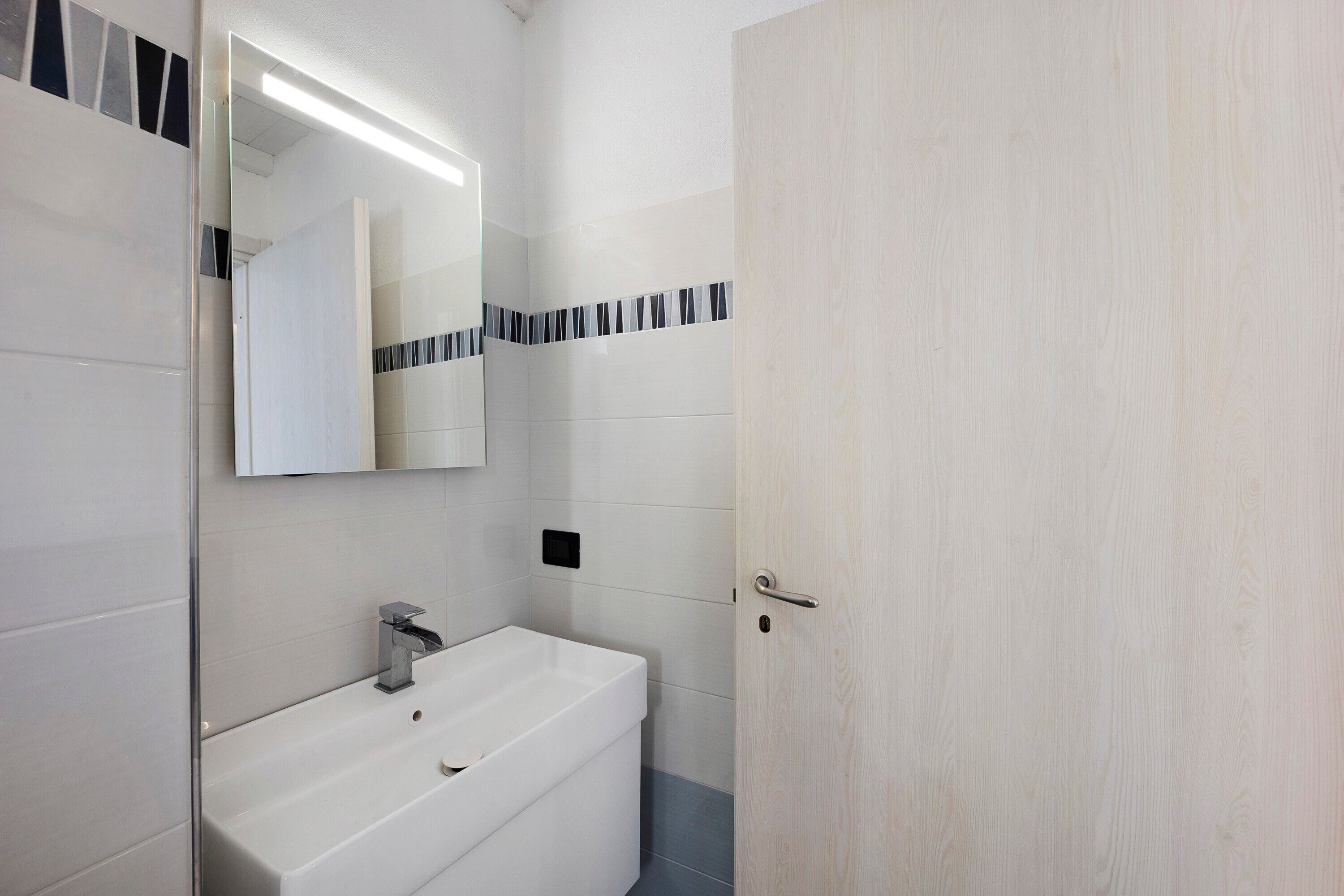 Une salle de bain avec un lavabo blanc, un miroir et une porte.