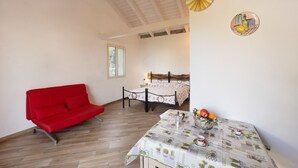 Una habitación con un sofá rojo, una cama con colcha estampada, una mesa con fruta y tazas, y decoración en la pared.