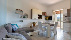 Ein modernes Wohnzimmer mit einer Couch, einem Esstisch, Stühlen und einer Küchenzeile mit Regalen und Blick.