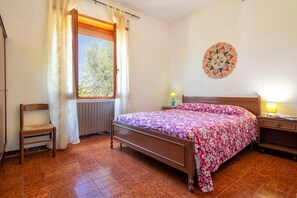 Ein Schlafzimmer mit einem hölzernen Bett, einem Sessel, einem Fenster mit Vorhängen, einer Wanddekoration und einer Nachttischlampe.