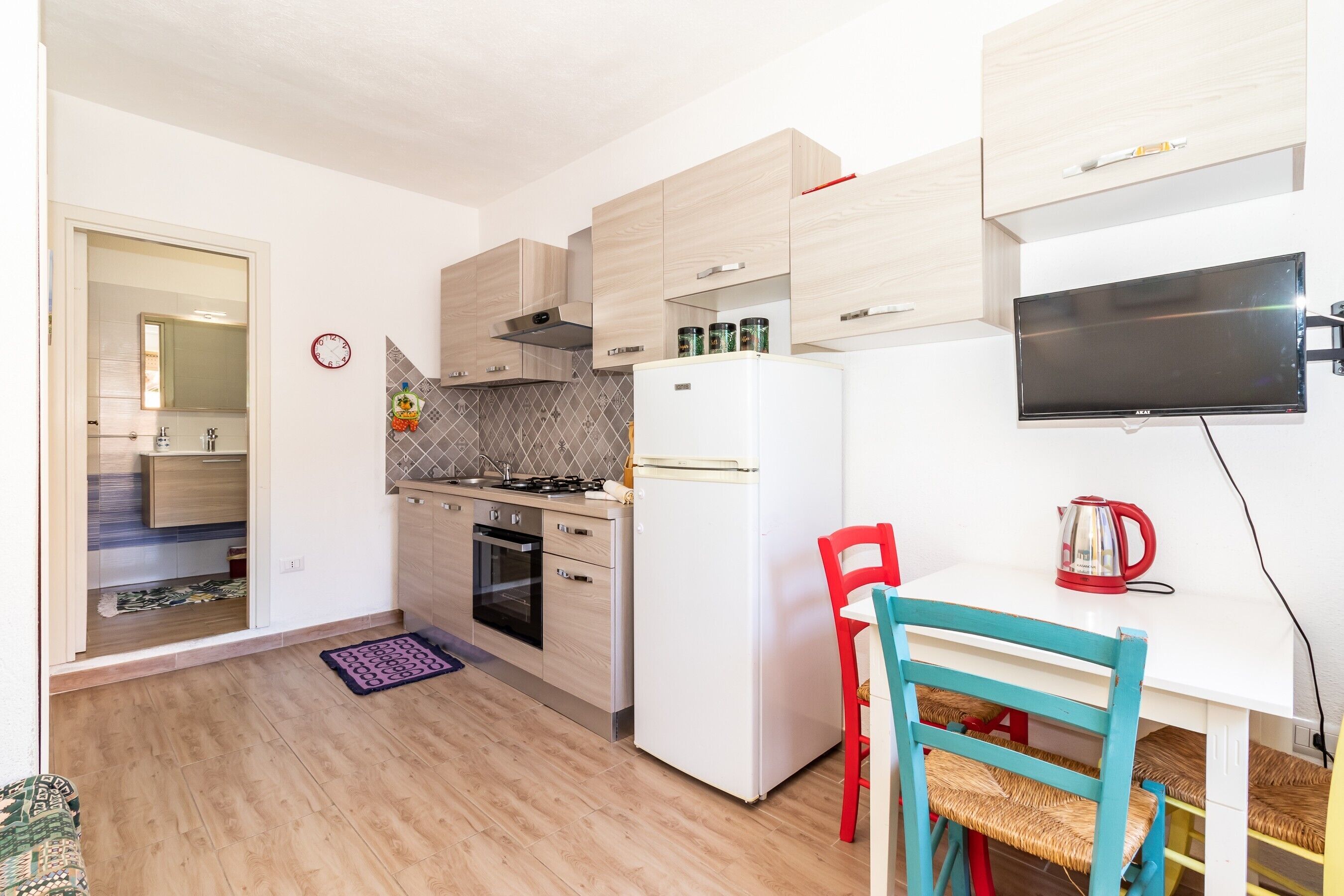 A compact kitchen with wooden cabinets, a white refrigerator, a stove, and a dining area with a table and chairs.