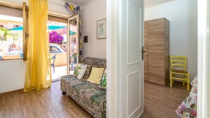A room with a patterned sofa, a wooden wardrobe, a yellow chair, and a door leading to an outdoor area with a yellow curtain.