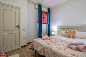 Une chambre à coucher avec un lit, des oreillers, une couette, une fenêtre avec des rideaux, une porte et une table de chevet.