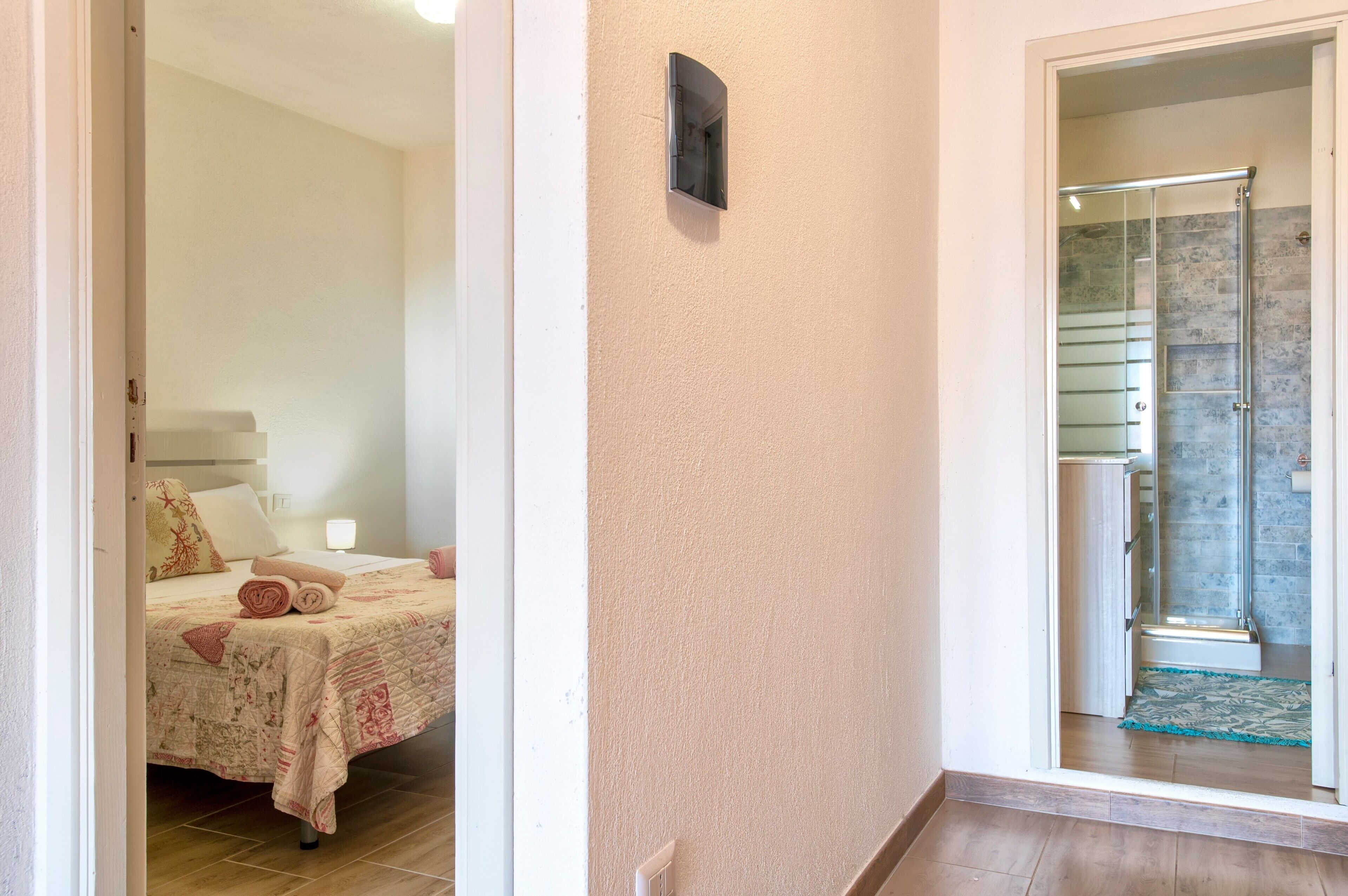 Una camera d'albergo con un letto, un bagno dotato di cabina doccia in vetro e un corridoio.
