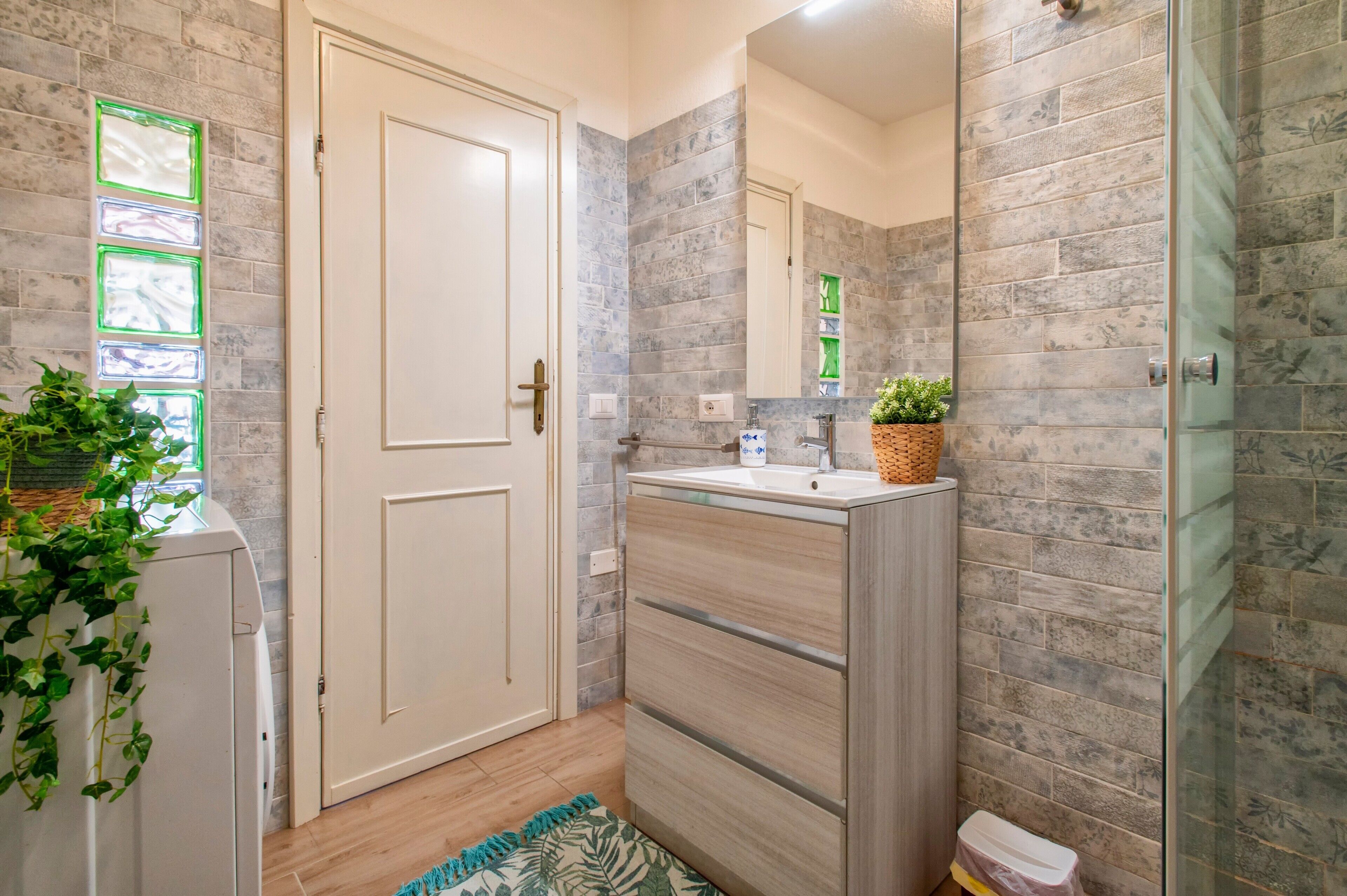 Een badkamer met een witte deur, een wastafel met spiegel en een douche.