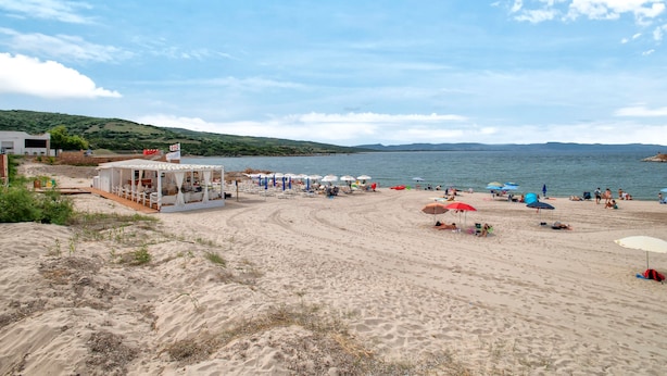 A beach with a white building, umbrellas, and people. - Apartment 'Endless Summer' with Sea View, A/C and Balcony (Isola Rossa)