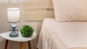 A neatly made bed with a white pillow and a round table with a lamp and a green plant beside it. - Apartment 'Endless Summer' with Sea View, A/C and Balcony (Isola Rossa)