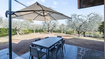 Un patio esterno con tavolo e sedie, un ombrellone grande e vista su alberi e un edificio.