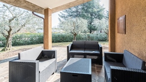 Une terrasse extérieure dotée de meubles en osier, d’un sol en pierre et offrant une vue sur les arbres et la verdure.