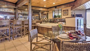 Un interior rústico con muebles de mimbre, una mesa de comedor con superficie de vidrio y una zona de bar con estantes llenos de botellas.