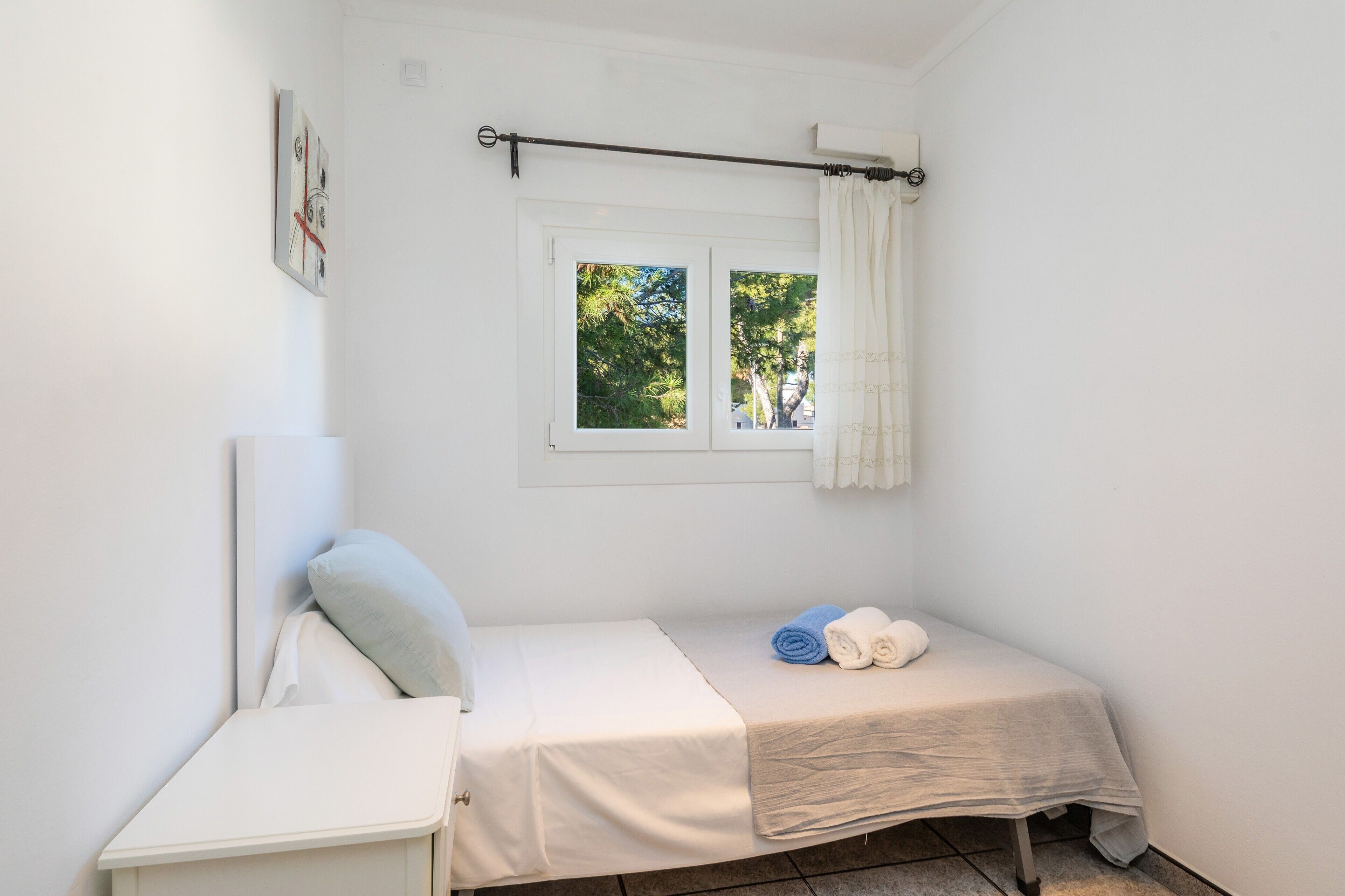 Una habitación pequeña y limpia con una cama individual, una ventana con cortinas y una obra de arte en la pared.