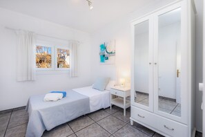 A bedroom with a bed, a nightstand, a wardrobe, a window with curtains, and a wall-mounted abstract art piece.