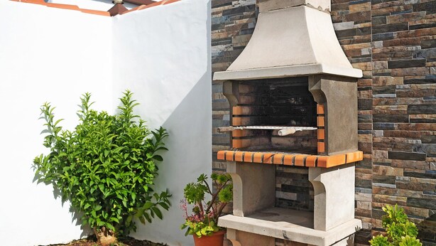 Een stenen barbecue met schoorsteen, een potplant en een bakstenen muur.