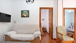 Een woonkamer met een bank, fauteuil, televisie en een schilderij aan de muur.