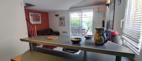 A kitchen with a long countertop, a dining area with a table and chairs, and a view of the outdoors through large windows.