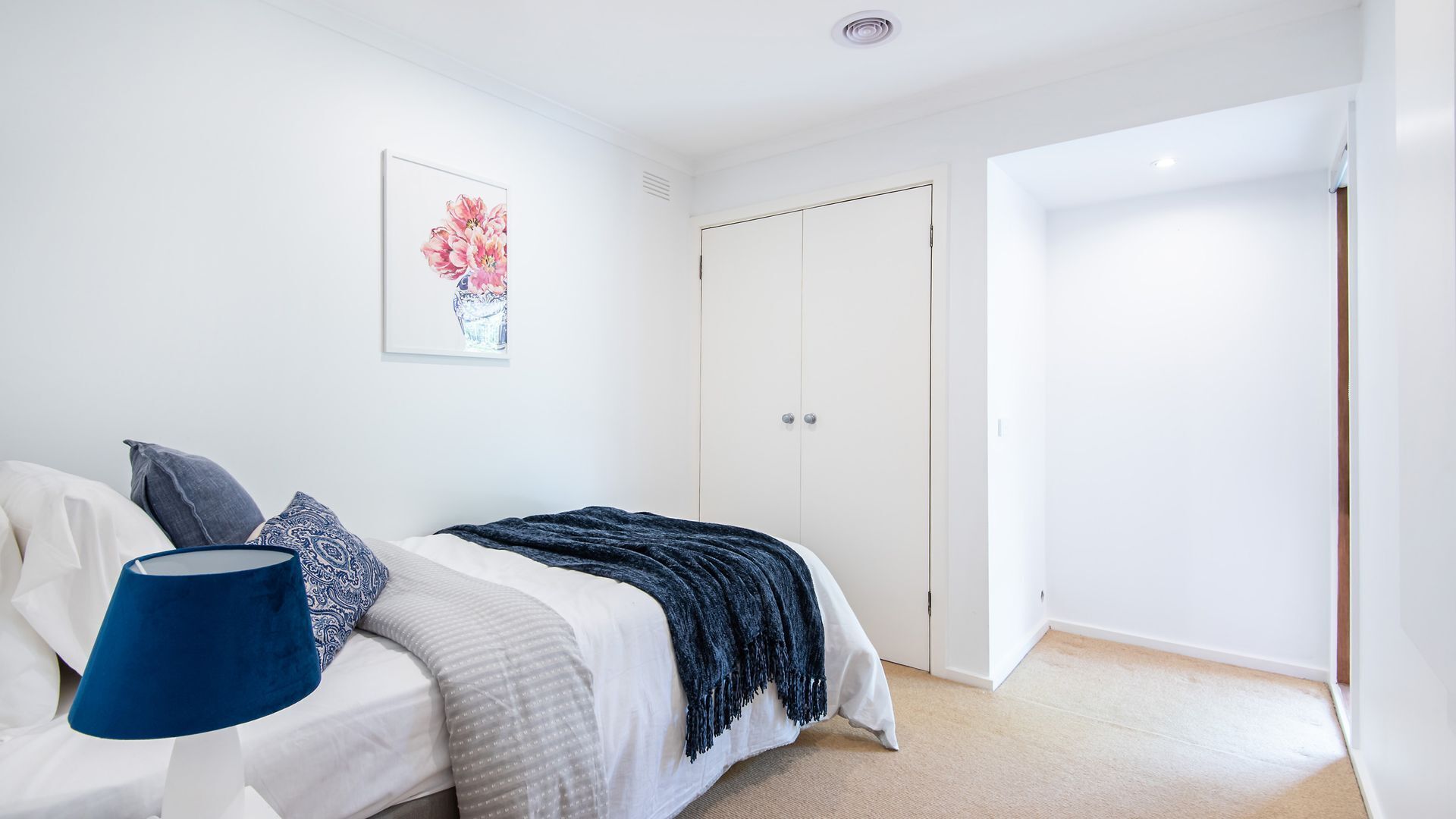 A bedroom with a bed, a bedside table with a lamp, a wardrobe, and a framed picture on the wall.