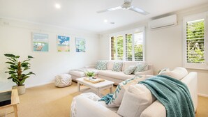 A modern living room with a sofa, coffee table, and decorative pillows. There are three framed pictures on the wall and a plant in a pot. - Pet Friendly - Preston Alfresco Poolside Retreat Rye (Rye)