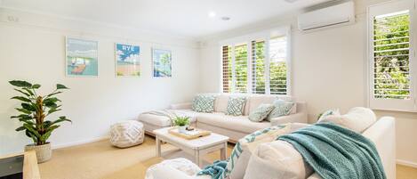 A modern living room with a sofa, coffee table, and decorative pillows. There are three framed pictures on the wall and a plant in a pot.