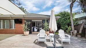 A wooden deck with white chairs and a table, a large potted plant, and a covered umbrella. - Pet Friendly - Preston Alfresco Poolside Retreat Rye (Rye)