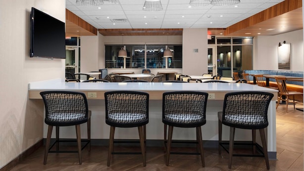 A modern bar area with a central island, bar stools, pendant lighting, and a flat-screen TV mounted on the wall. - Fairfield Inn & Suites by Marriott Winnemucca (Winnemucca)