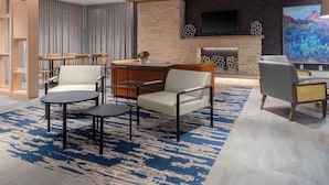 A modern living room with a stone fireplace, a flat-screen TV mounted above it, and a large painting on the wall. - Fairfield Inn & Suites by Marriott Winnemucca (Winnemucca)