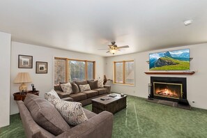 A living room with a sofa set, a fireplace, a television mounted above the fireplace, and a ceiling fan.