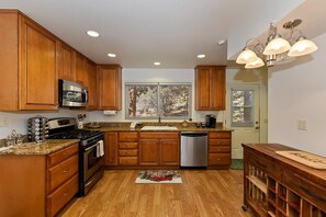 A kitchen with wooden cabinets, a stainless steel stove, a dishwasher, and a window with blinds.