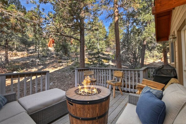 A deck with a fire pit, outdoor furniture, and a view of a forest.