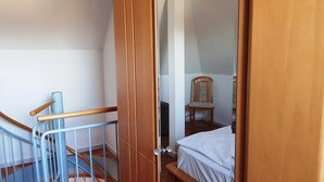Una habitación con puerta de madera, una silla, una cama y una escalera.