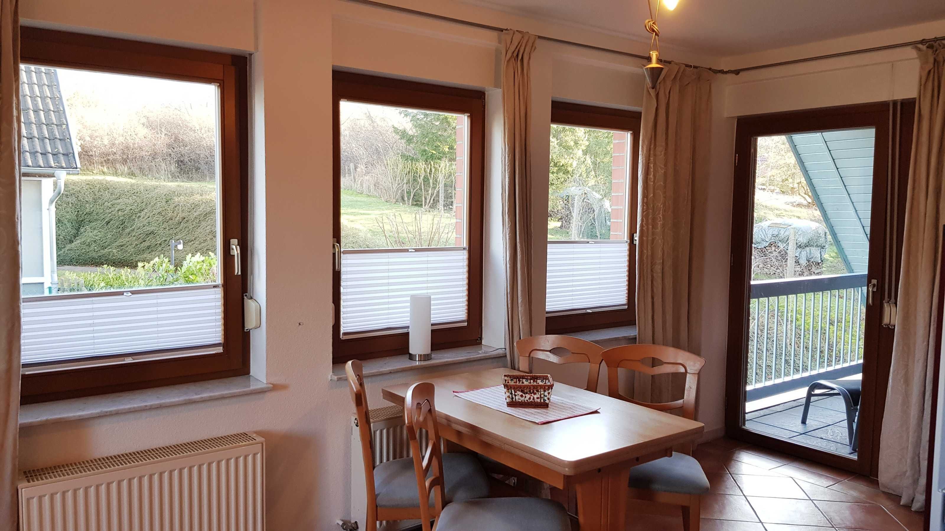 Een eetruimte met een tafel, stoelen, grote ramen, een radiator en uitzicht op buiten.