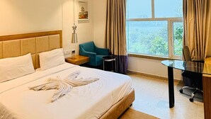 A hotel room with a large bed, a desk, a chair, a window with curtains, and a ceiling fan. - Hotel Amora (Rajnandgaon)