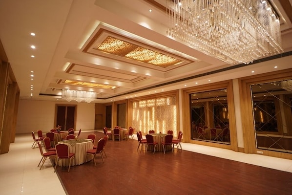 Une salle de banquet spacieuse, avec des tables rondes et des chaises rouges, un grand lustre et un mur décoré d’un motif original.