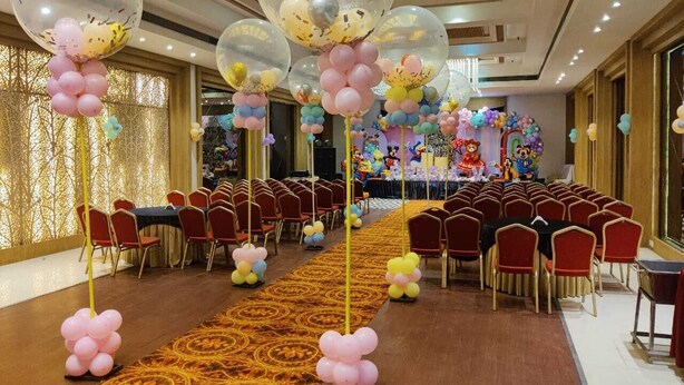 A banquet hall with rows of red chairs, a long table in the center, and balloons hanging from the ceiling. - Hotel Amora (Rajnandgaon)