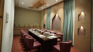 A conference room with a long table, red chairs, and a chandelier. - Hotel Amora (Rajnandgaon)