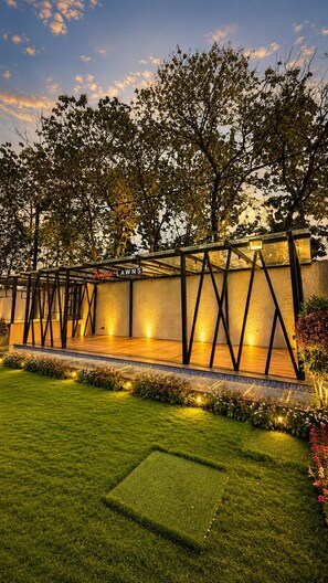 An outdoor garden area with a well-lit pathway, a seating area, and a wall with a name sign. - Hotel Amora (Rajnandgaon)