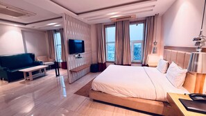 Habitació d'hotel amb un llit gran, televisió, sofà i escriptori amb làmpada.