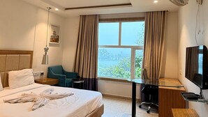 A hotel room with a large bed, a desk, a chair, a TV, and a window with a view. - Hotel Amora (Rajnandgaon)