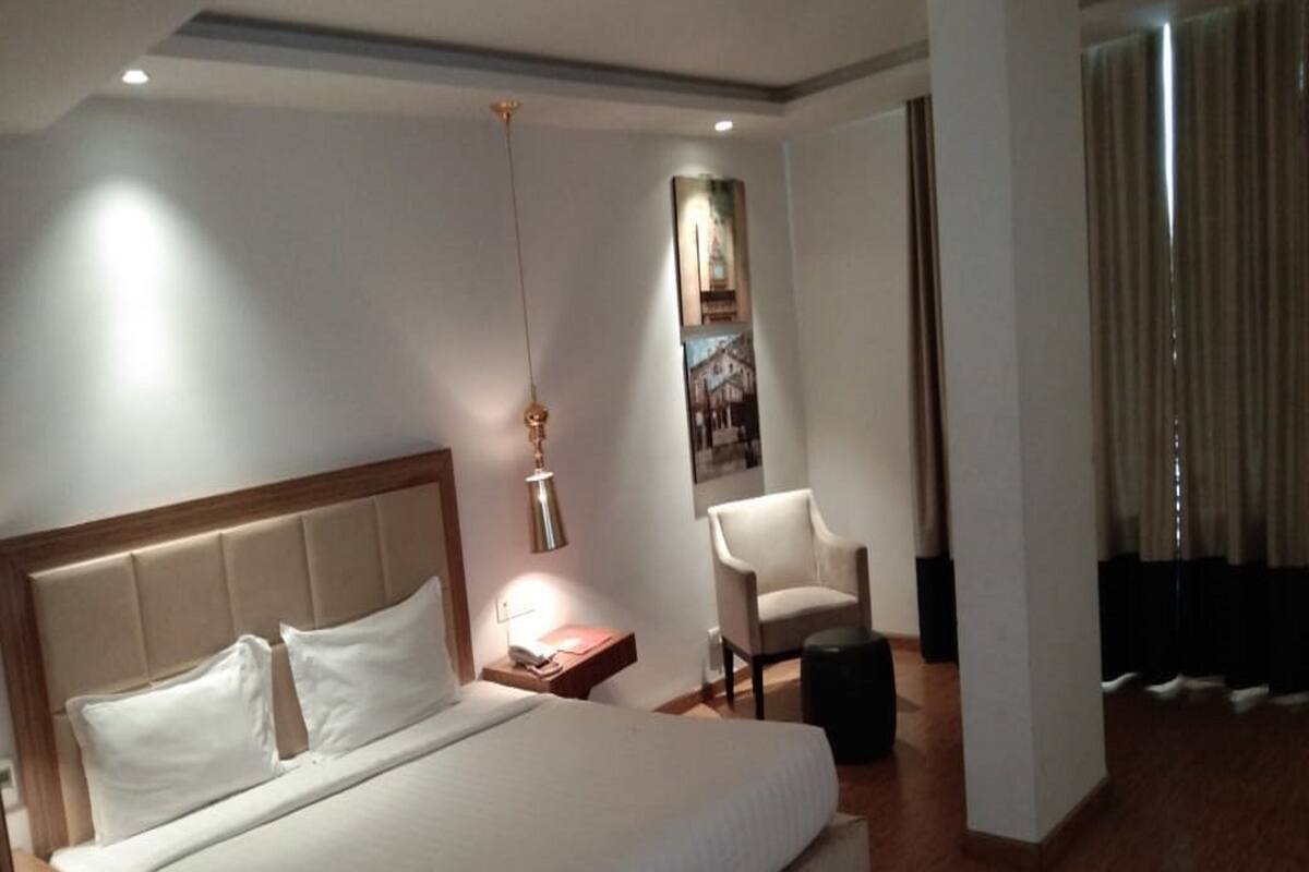 Une chambre d’hôtel avec un grand lit, une table de chevet avec une lampe, une chaise et une affiche au mur.